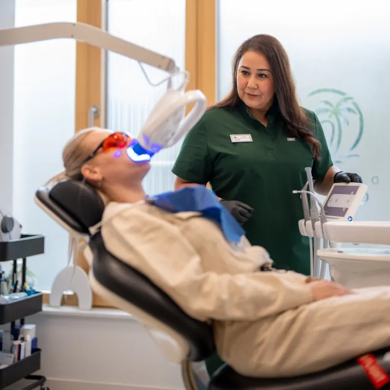 Bleaching-Behandlung in der Dentale Oase: Patientin mit Schutzbrille unter der Aufhellungslampe, behandelnde Zahnärztin daneben